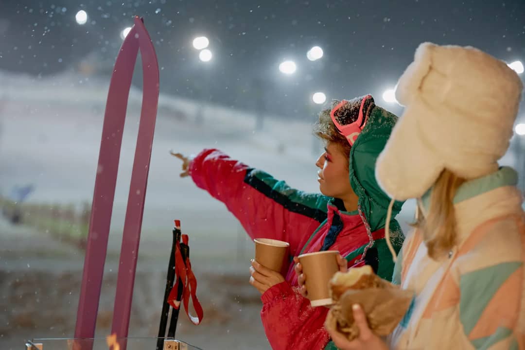 Two friends enjoying a warm drink while skiing on a snowy winter night.