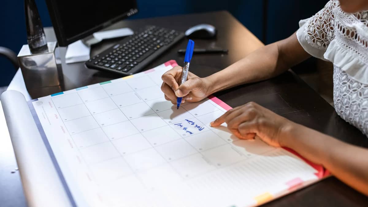 A person marking dates on a desk calendar with a pen — planning leave around the 2027 federal holidays