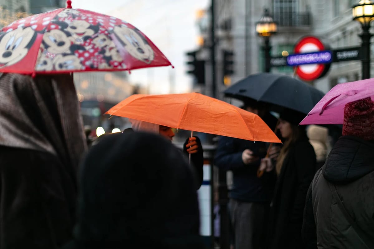 Colourful umbrellas crowding a rainy London street outside an Underground station