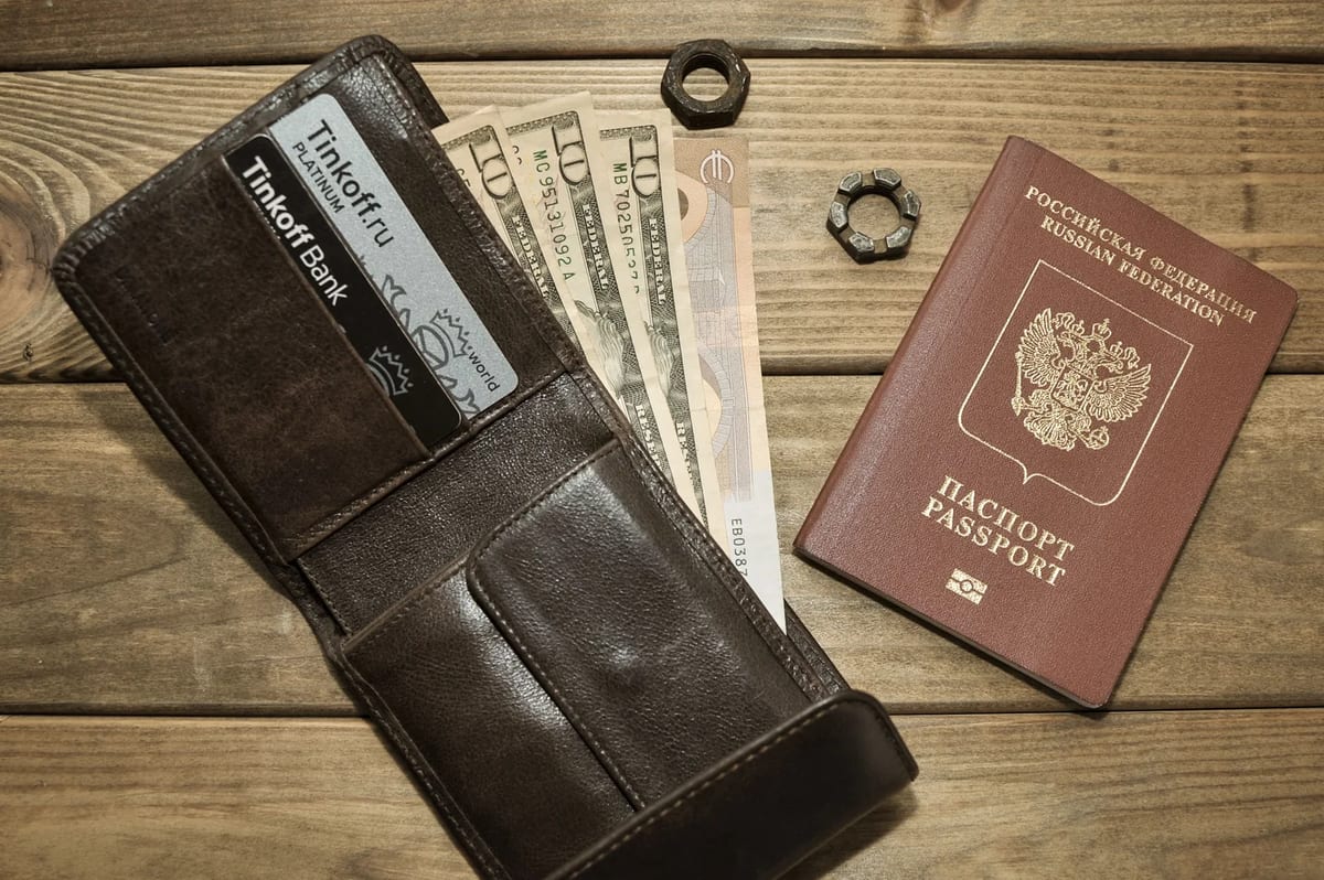 A brown leather wallet with cards, banknotes in several currencies and a passport on a wooden surface