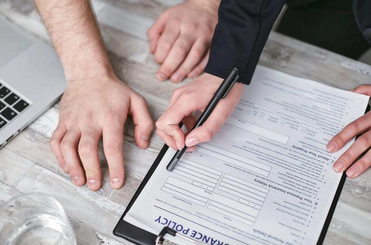 Two people signing an insurance policy document on a wooden desk