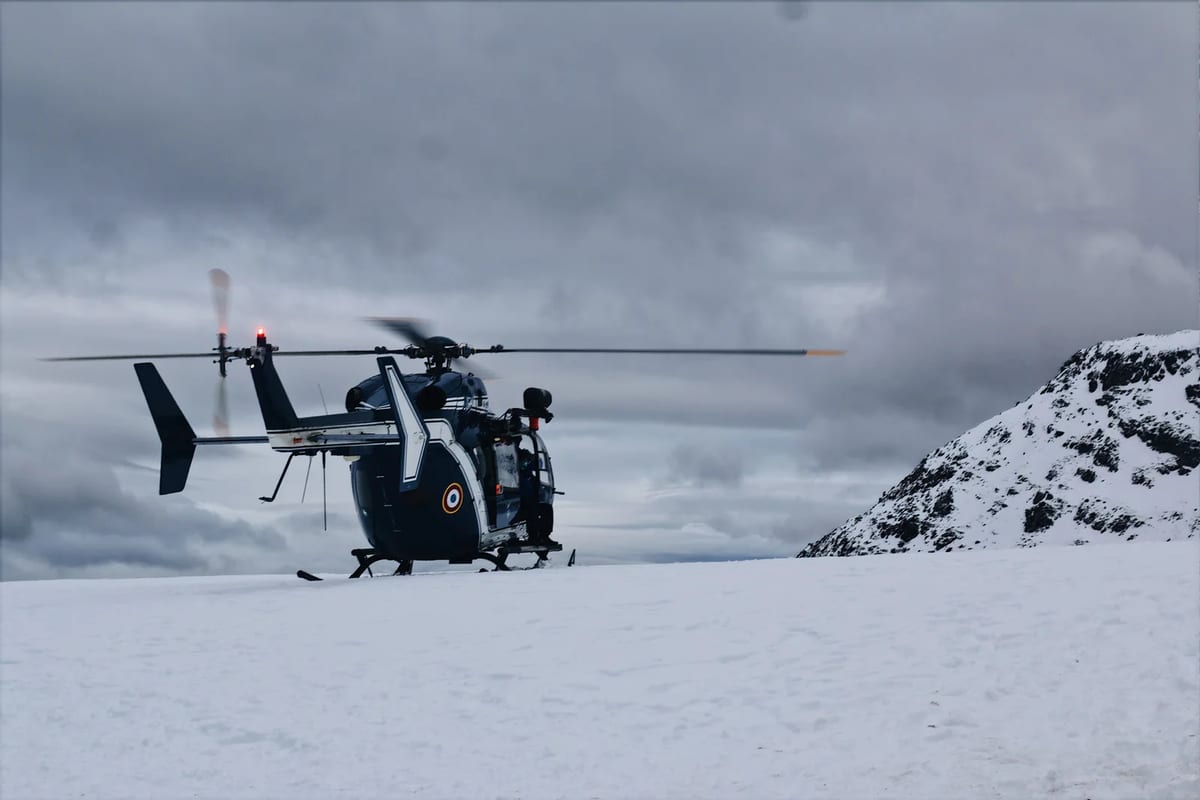 A helicopter landing in a snowy mountain setting under overcast skies