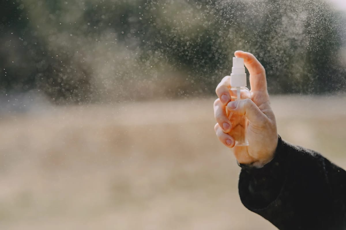 A hand holding a small spray bottle and spraying outdoors