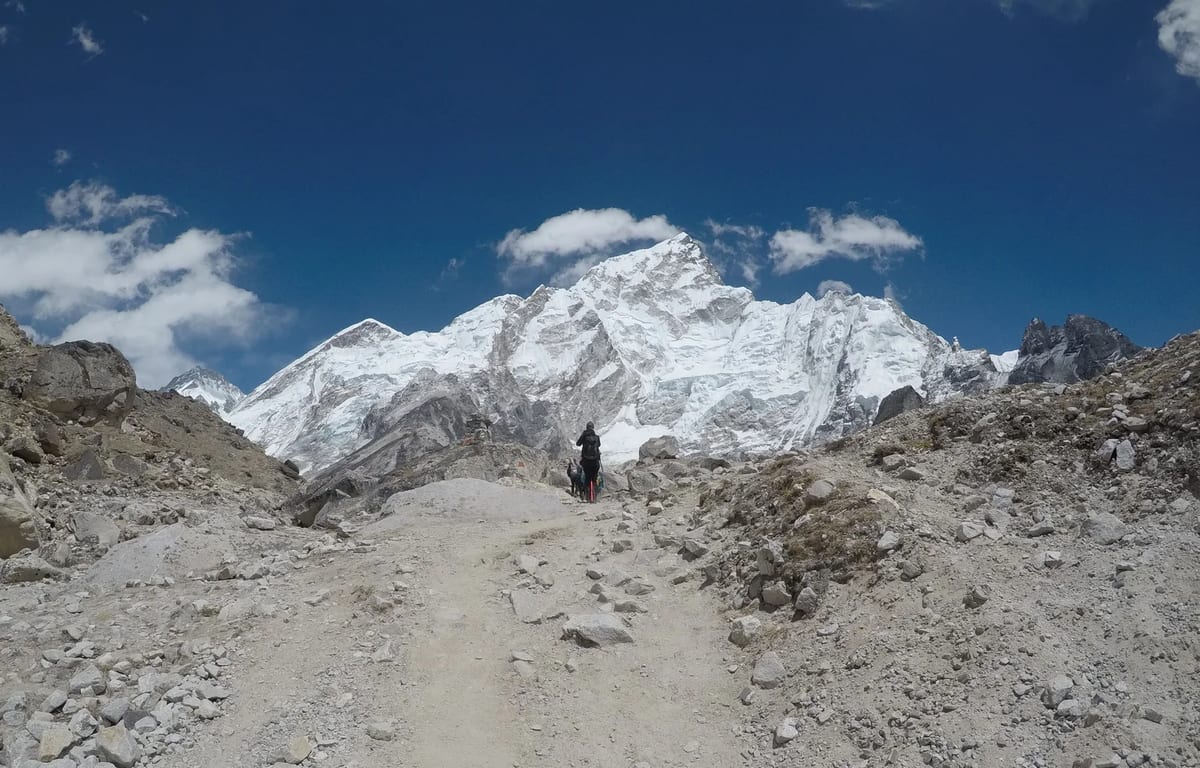 A lone trekker on a rocky path with snow-covered Himalayan peaks behind