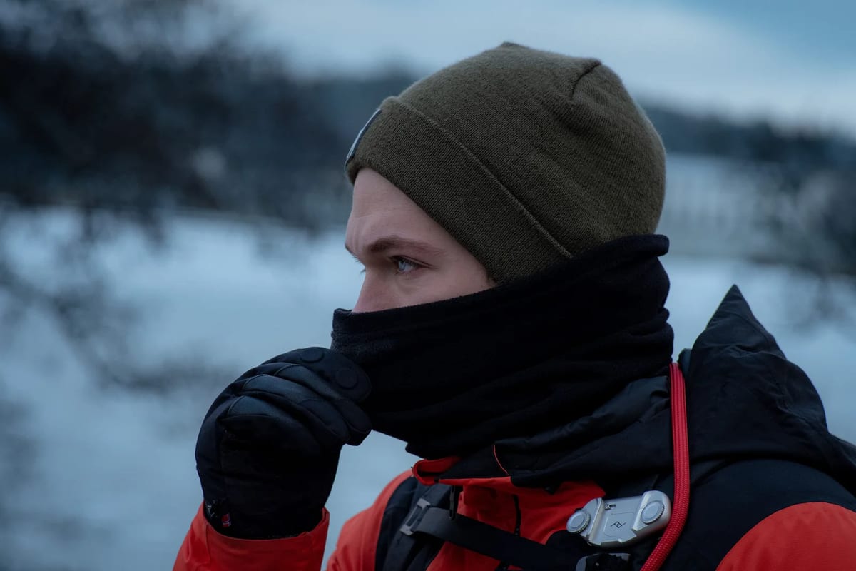 Man in a beanie pulling a black neck gaiter over his face against the cold