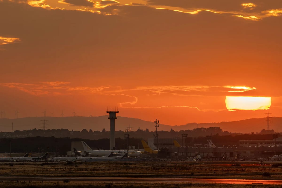 Airport control tower and parked aircraft silhouetted against an orange sunset