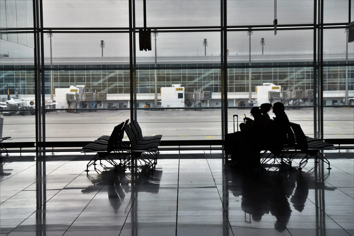 Silhouetted passengers waiting with luggage by large airport terminal windows