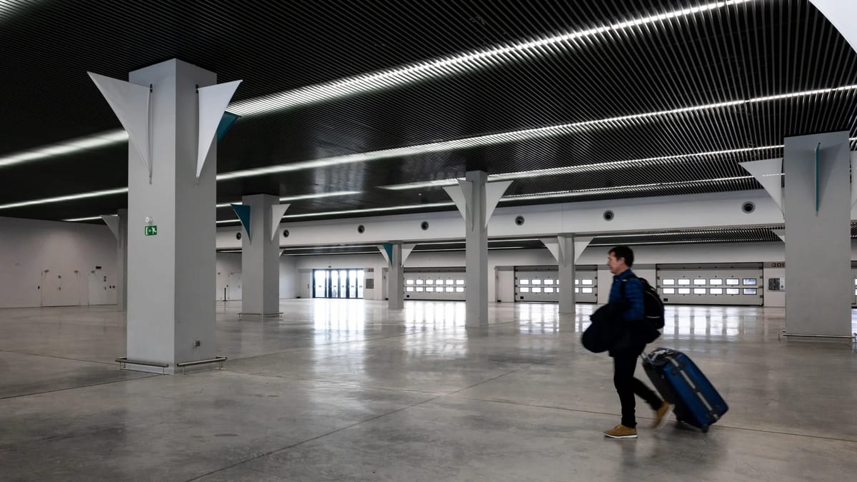 Passenger pulling a blue suitcase through a wide, empty airport hall