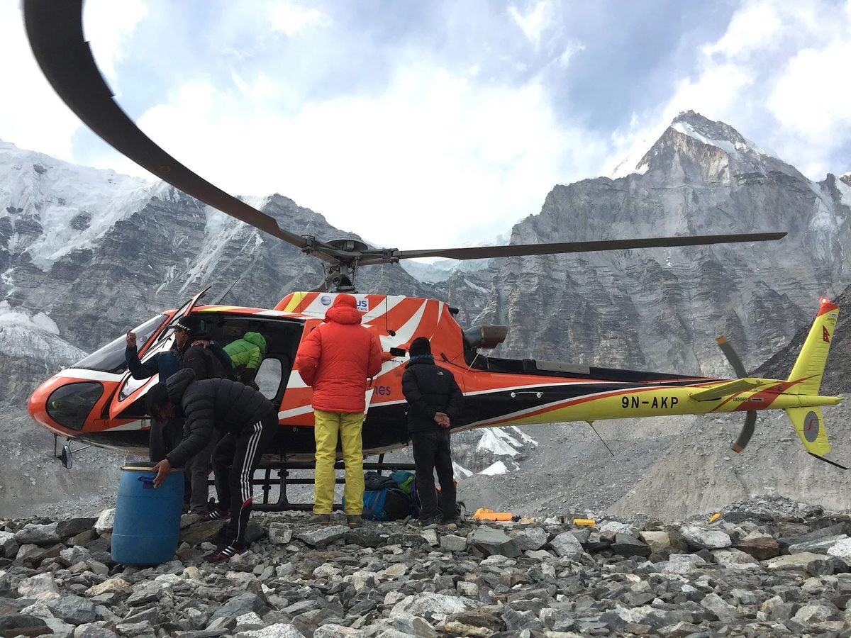A helicopter on rocky ground in the Himalaya with climbers standing beside it