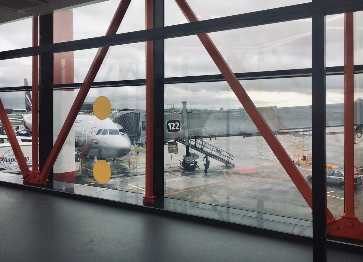 Aircraft parked at a terminal gate seen through tall glass windows with red steel frames