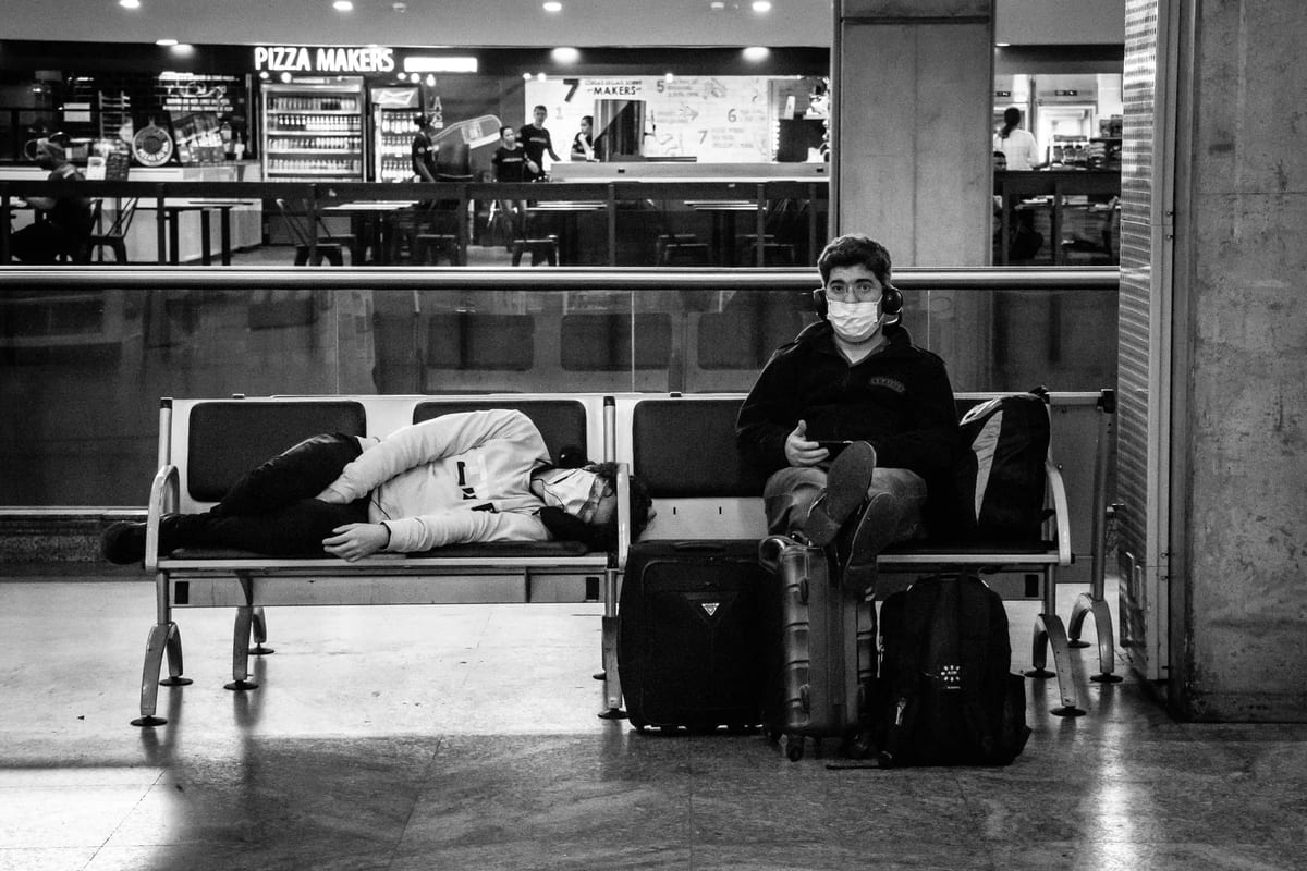 Black and white photo of travellers resting on a bench in a station hall with their luggage
