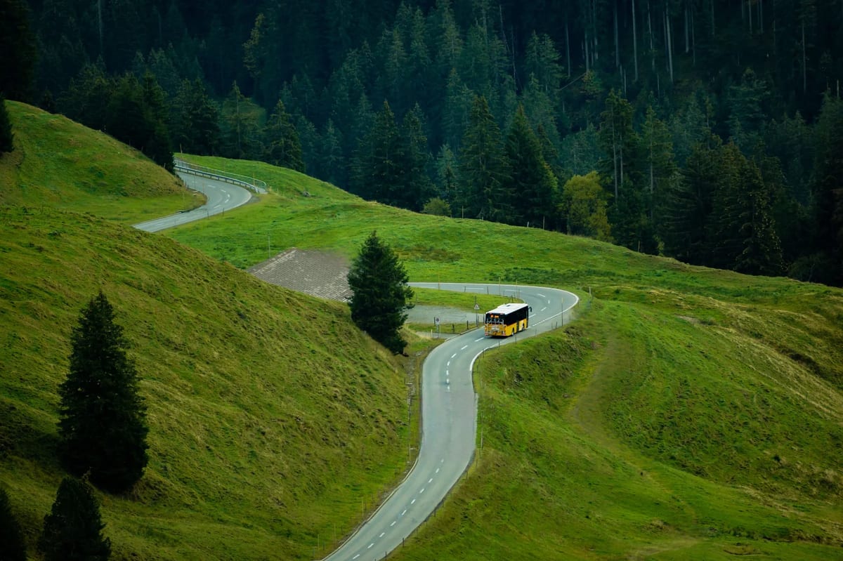 A bus climbing a winding road through green hills and forest