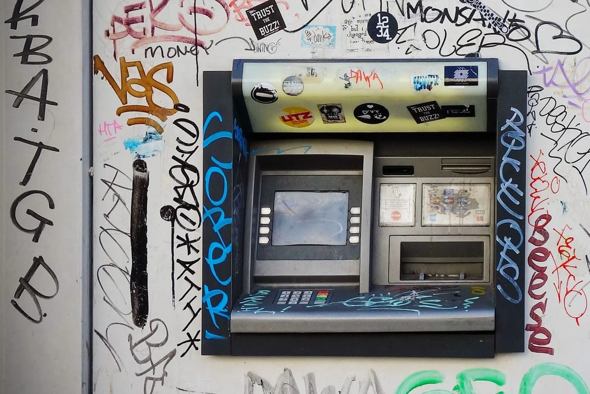 A cash machine set into a street wall covered in graffiti