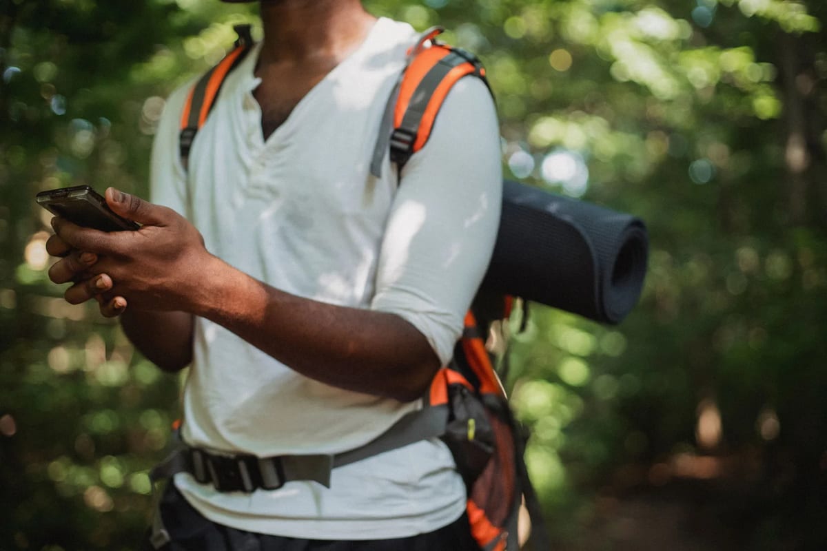 A hiker with a backpack checking a handheld device on a forest trail