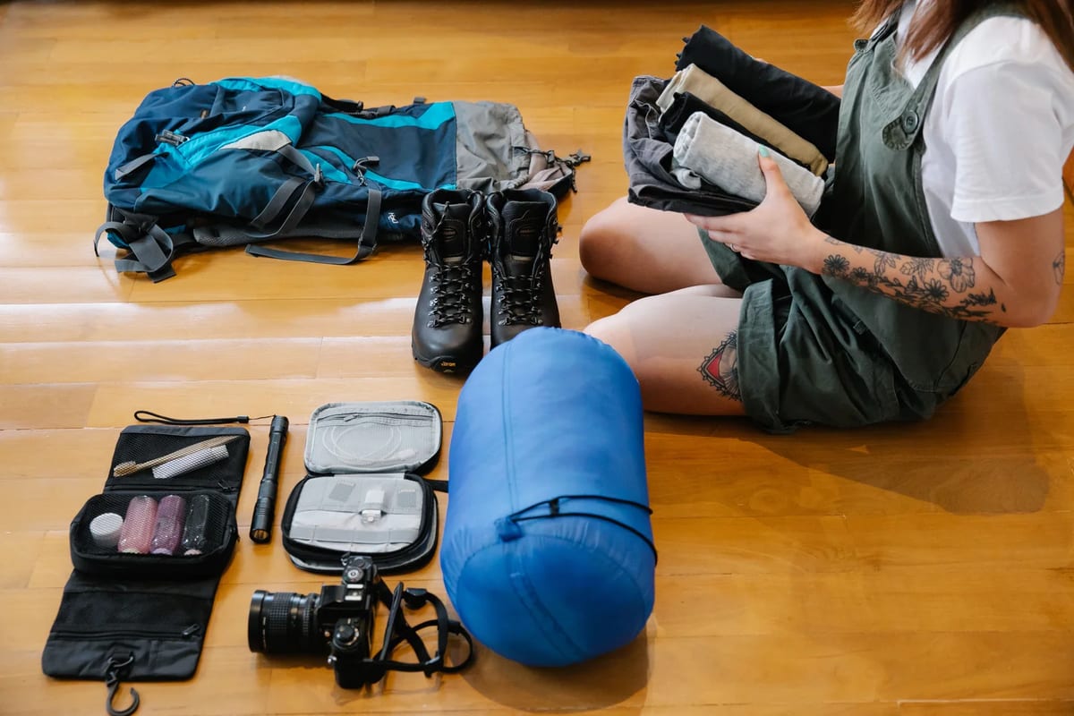 A traveller sorting trekking gear and clothes on a wooden floor before a trip