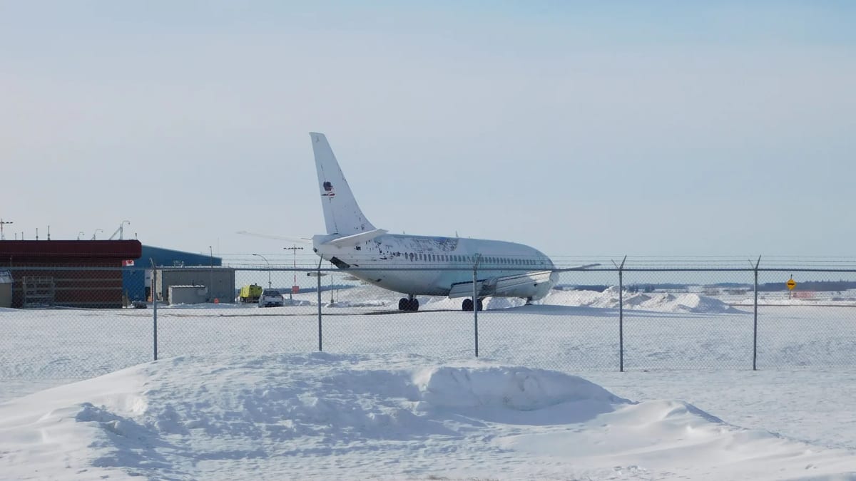 Passenger jet parked on a snow-covered apron behind an airport fence