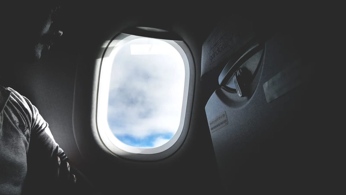 Silhouette of a passenger looking out of an aircraft window at the clouds