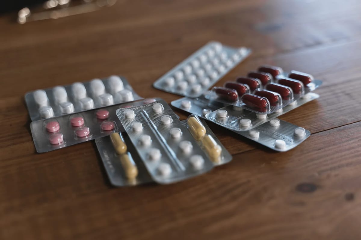 Blister packs of assorted tablets and capsules on a wooden table