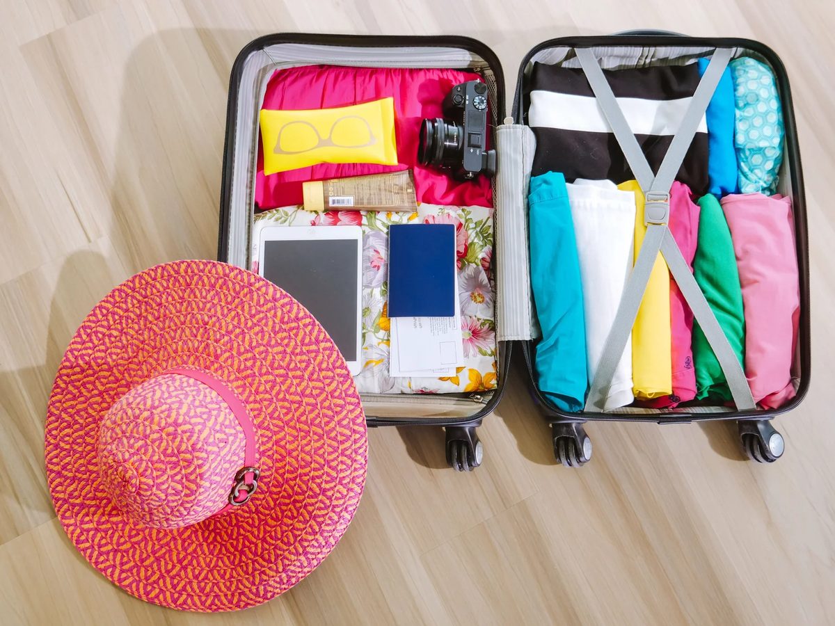 Open suitcase packed with clothes, a camera and a sun hat seen from above