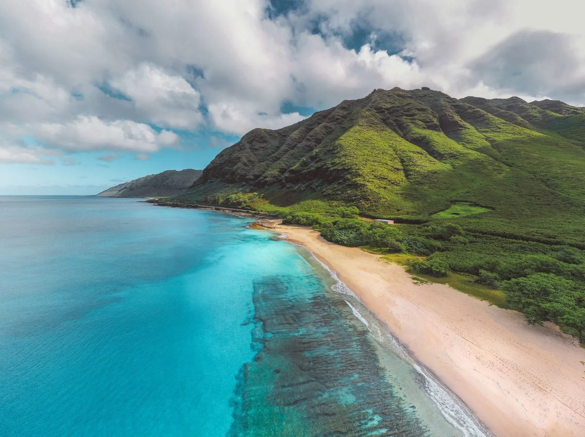 Aerial view of a Hawaiian beach below green mountains and a turquoise reef