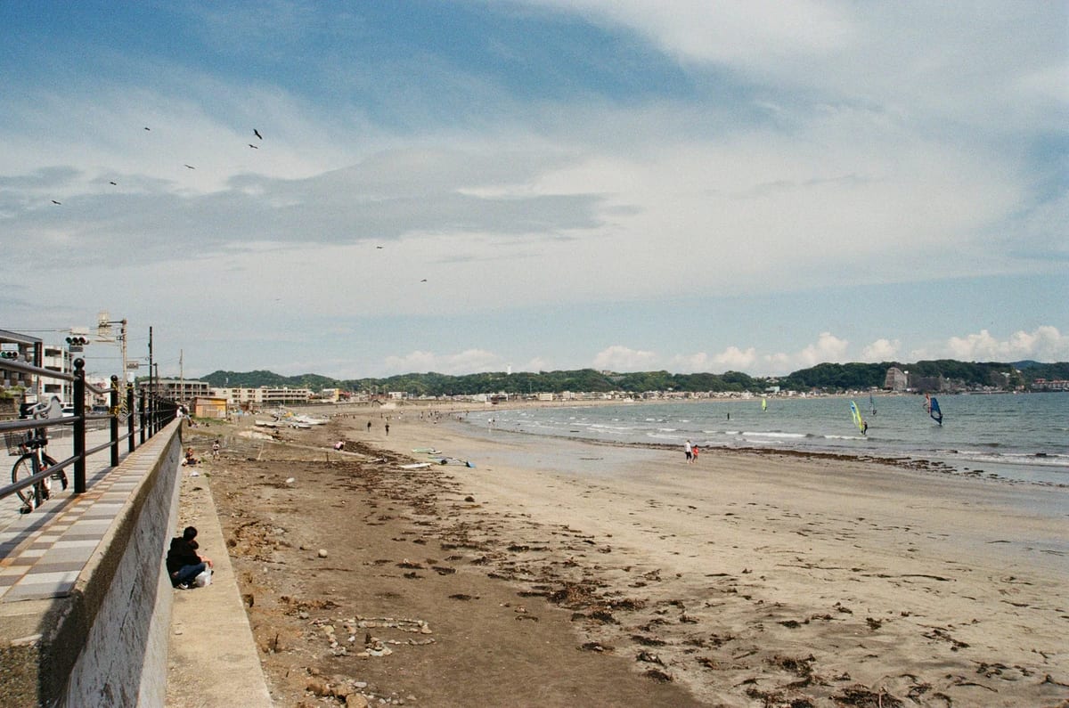 Wide sandy beach at Kamakura, Japan, with a seawall and windsurfers offshore