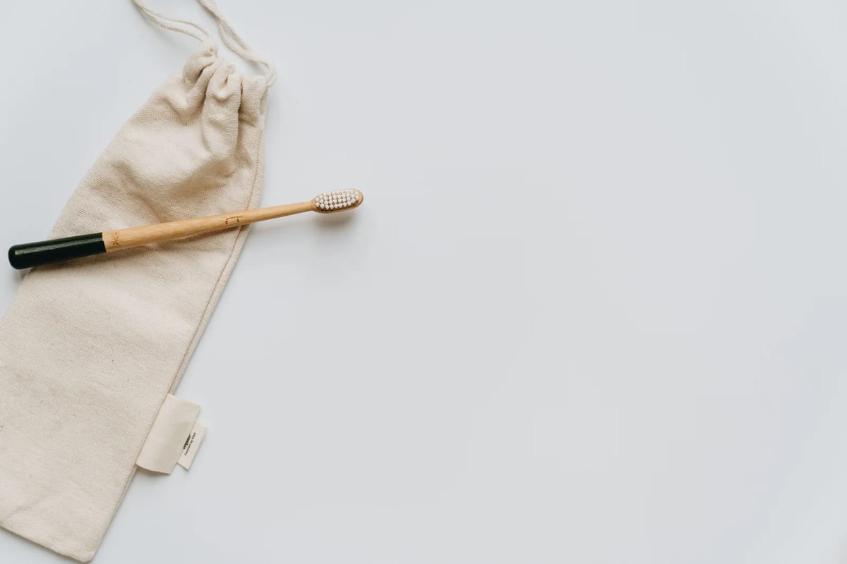A beige fabric toiletry bag beside a wooden toothbrush