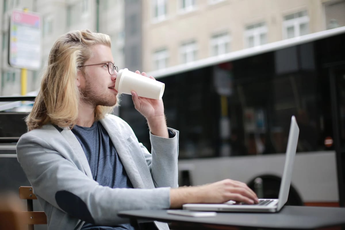 Man working on a laptop outdoors with a coffee
