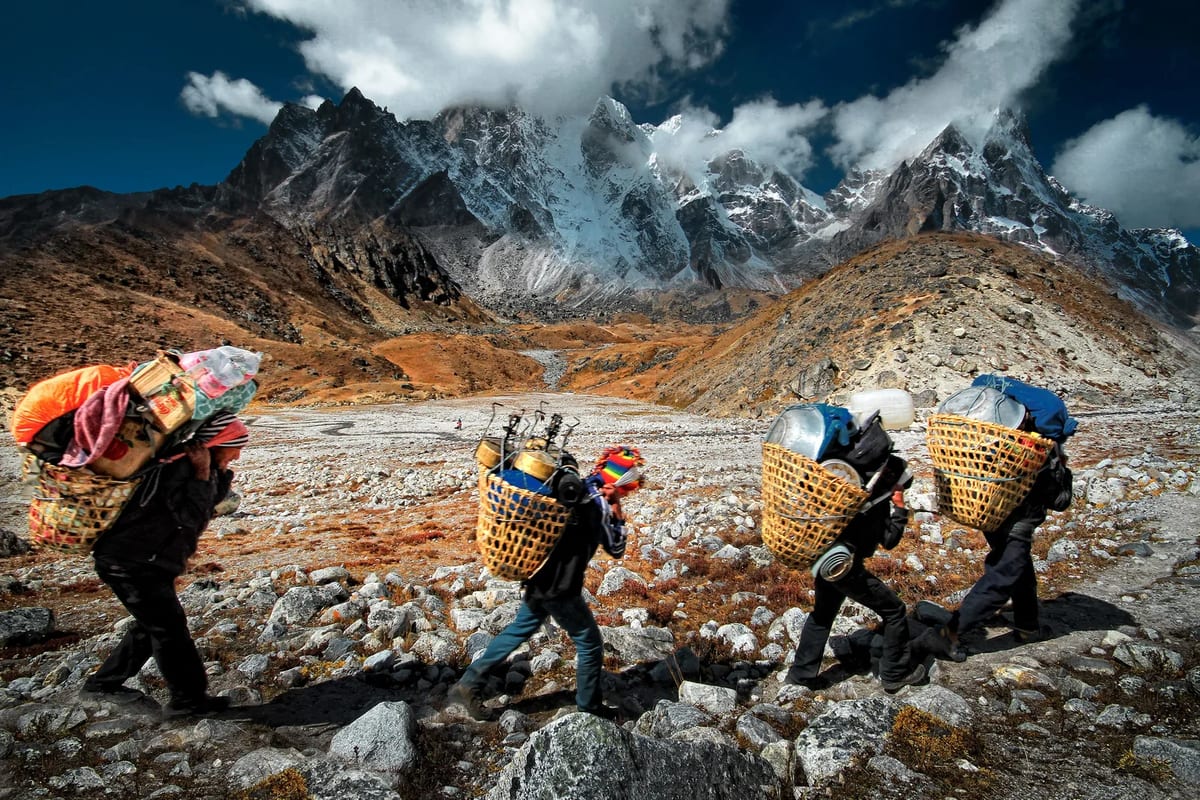 Porters carrying loads on a rugged Himalayan trail in Nepal with mountains behind