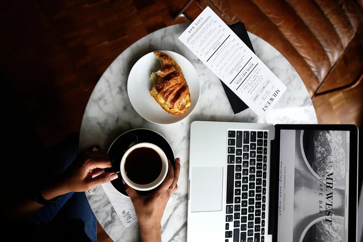 A laptop, coffee and a croissant on a cafe table