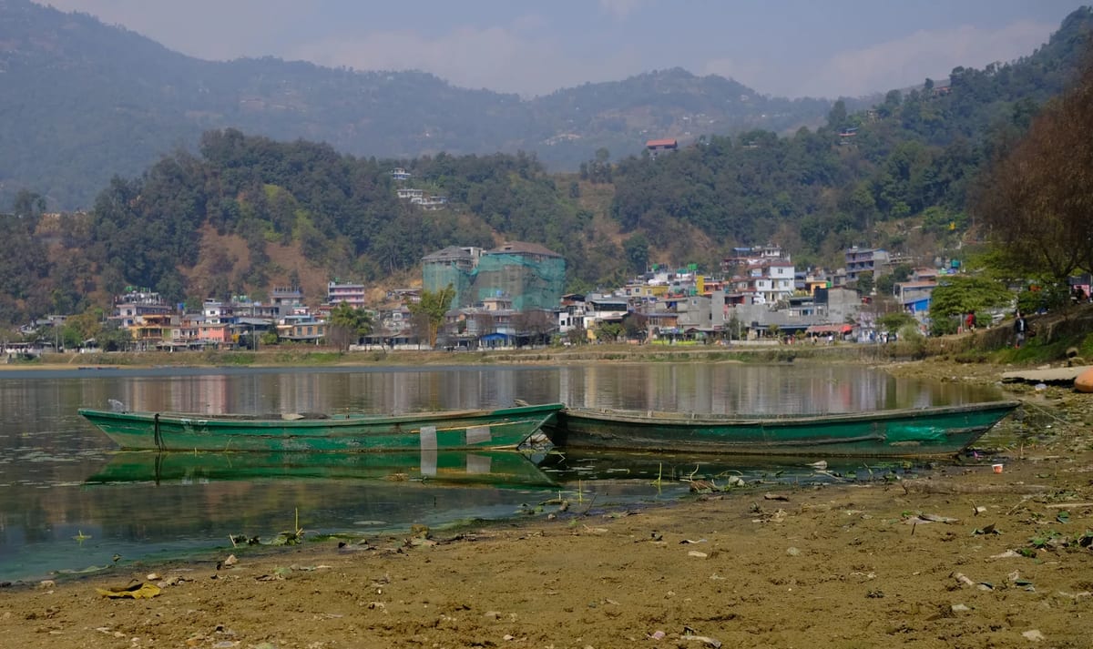 Boats moored on Phewa Lake with the town of Pokhara and green hills beyond