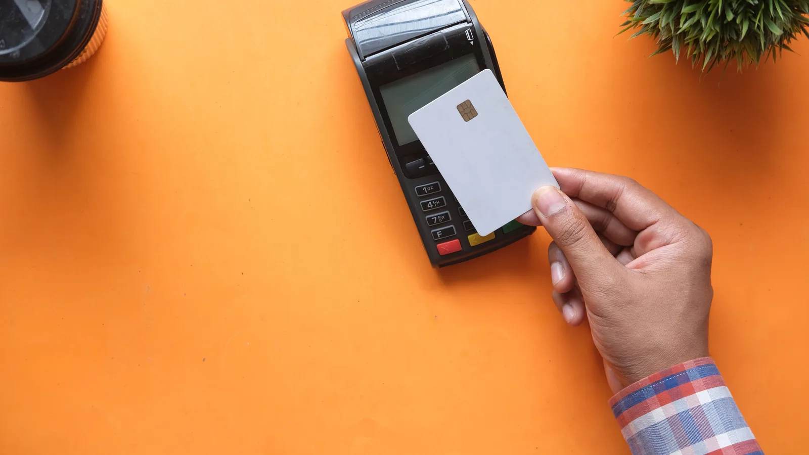 A hand holding a plain white chip card to a black card payment terminal on a bright orange desk