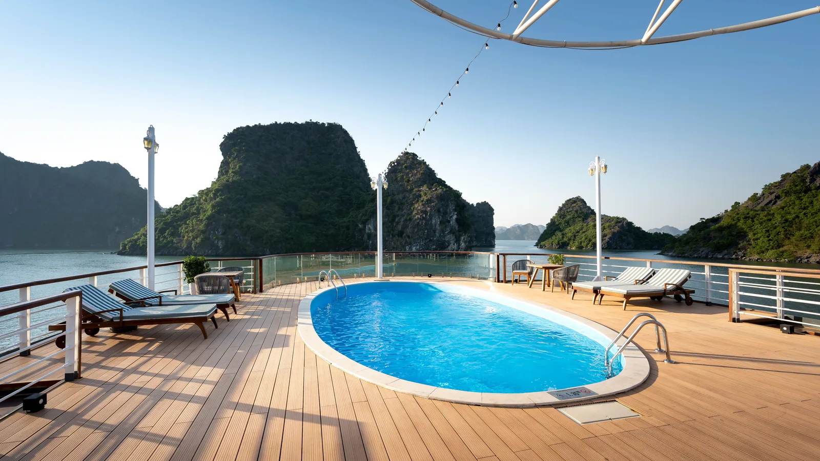 A cruise ship sun deck with a pool and loungers among limestone islands in Ha Long Bay