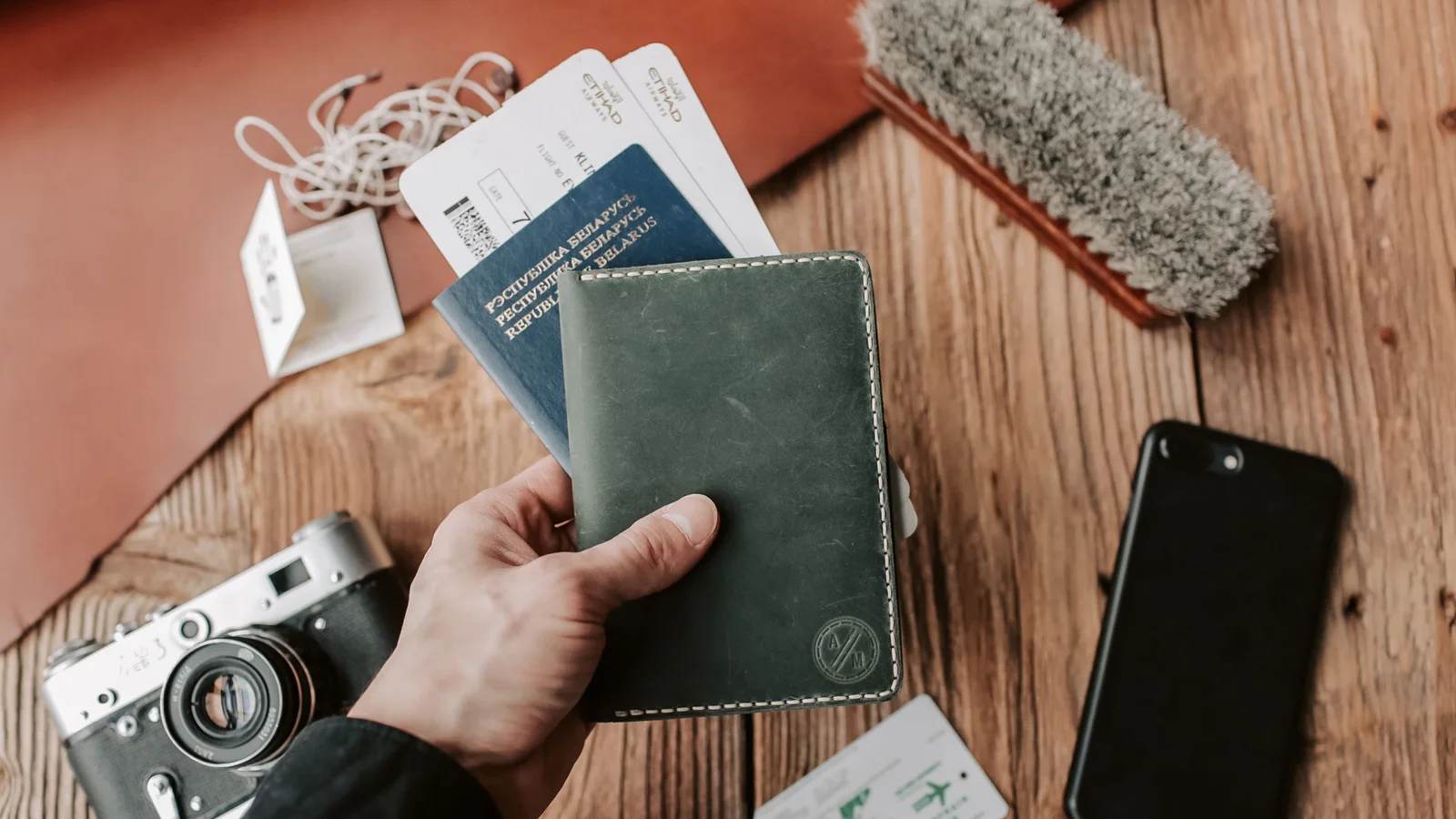 A hand holding a passport beside a camera and phone
