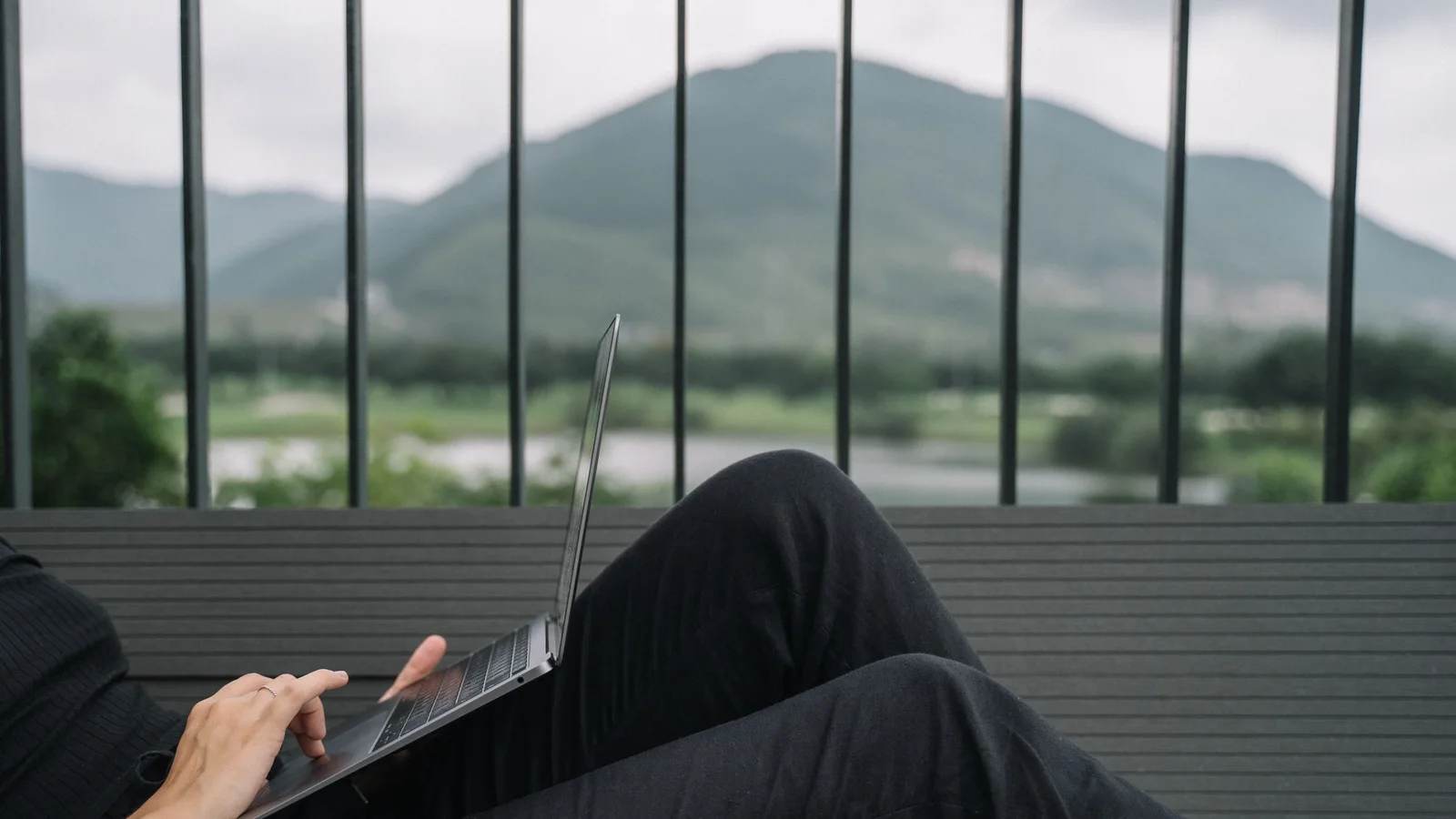 Person working on a laptop on a balcony facing mountains
