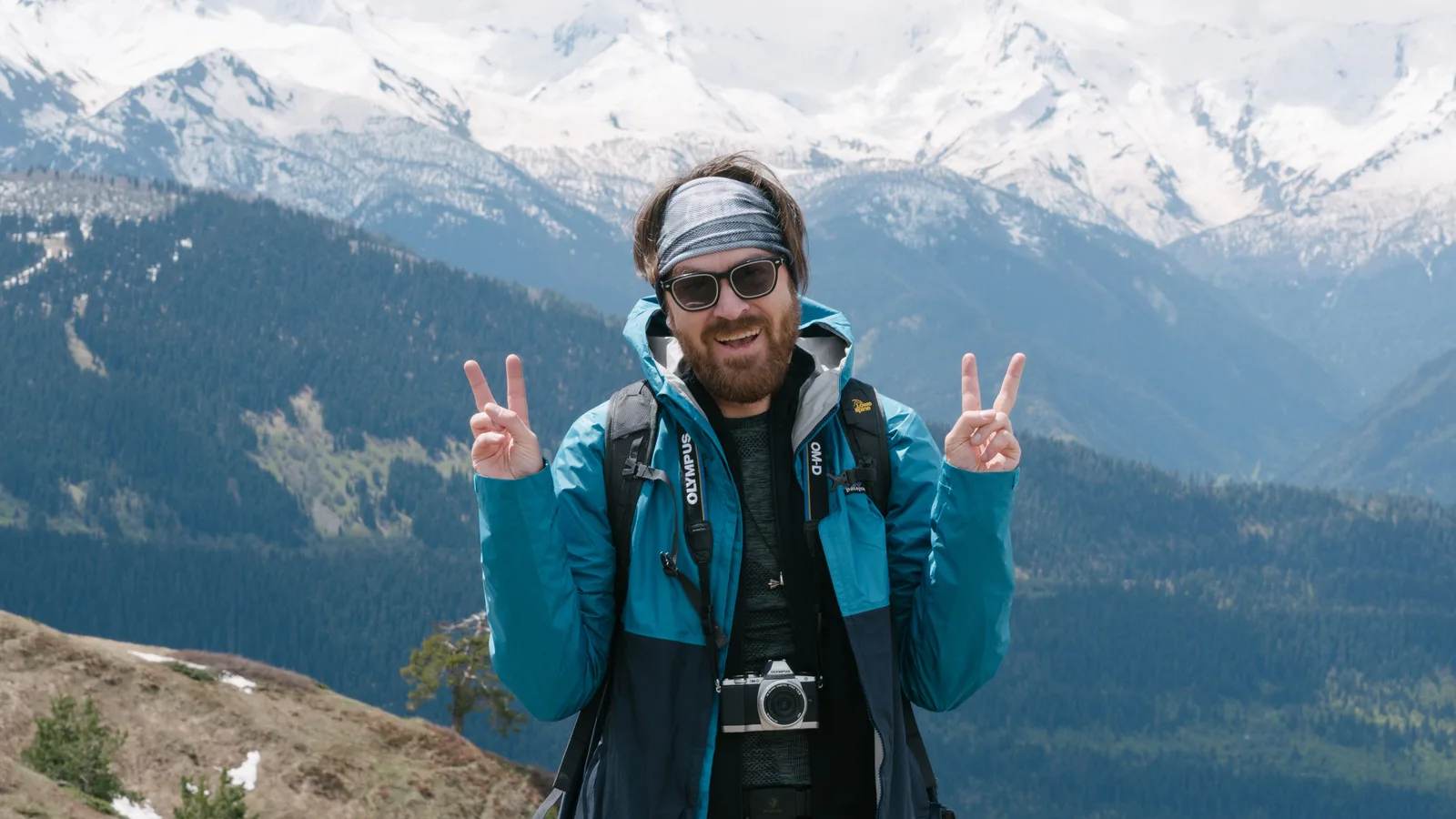 A hiker in sunglasses and a headband in front of snowy peaks