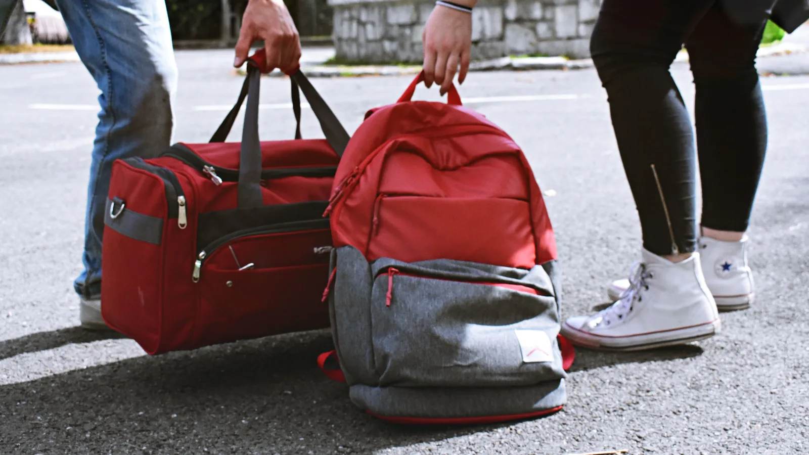 Two travellers carrying a red duffel and a backpack