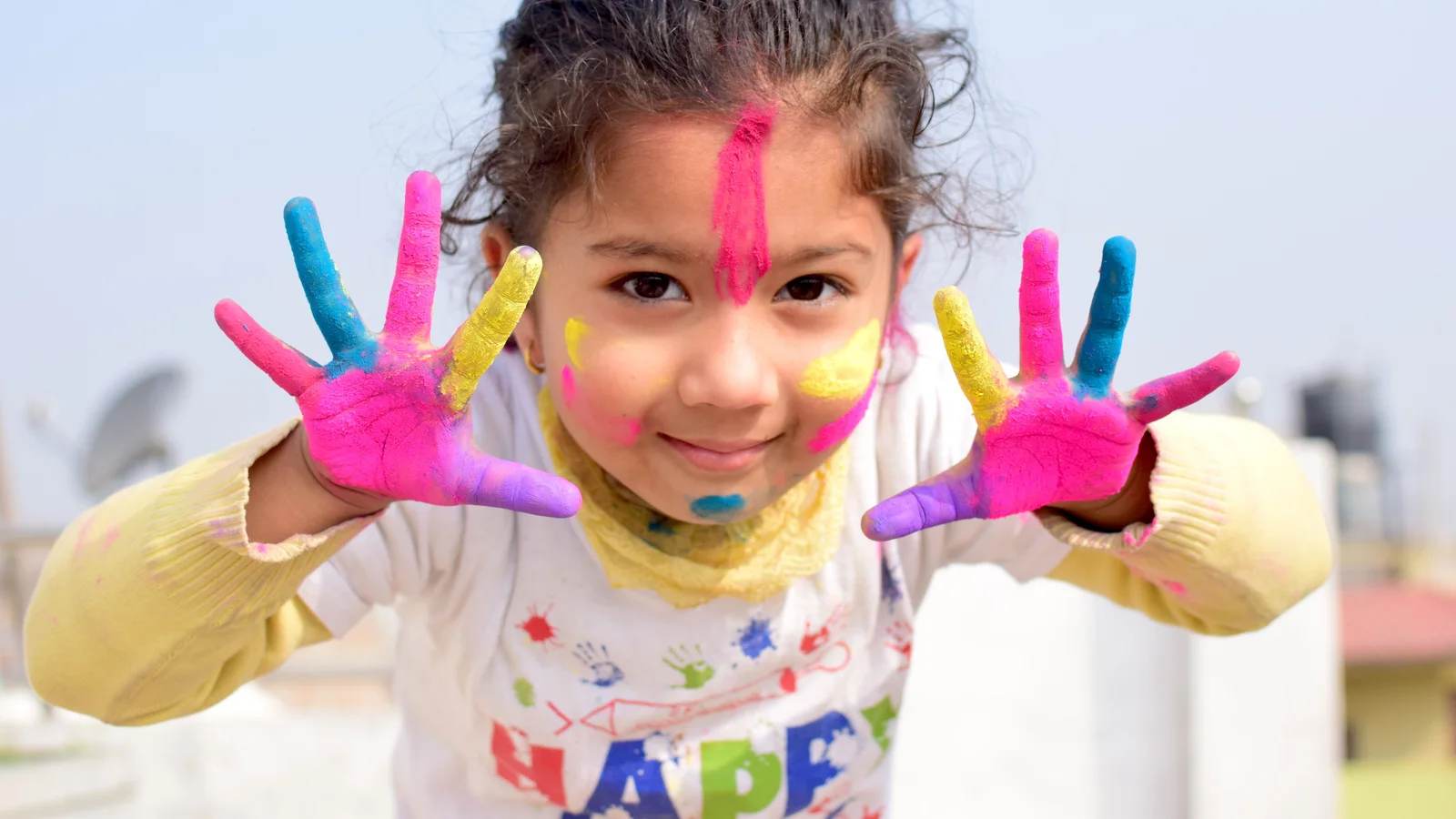 A smiling girl holding up hands covered in Holi colours in Bhaktapur, Nepal
