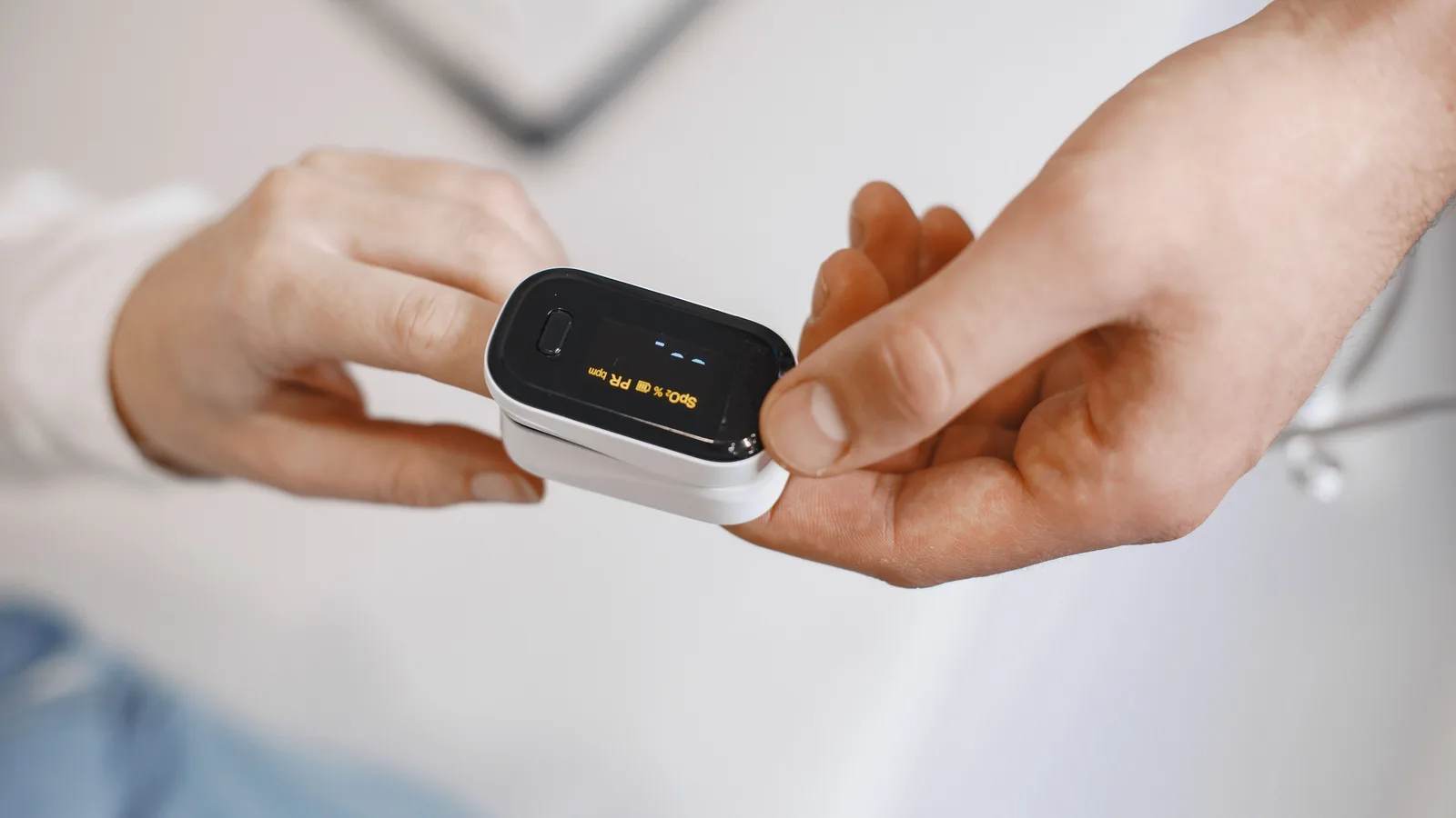 A pulse oximeter clipped to a fingertip showing an oxygen reading