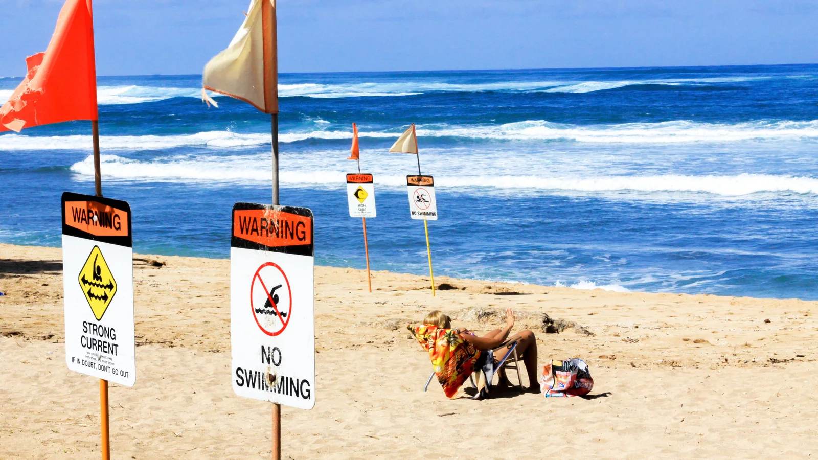 Strong current and no swimming warning signs with red flags on a sunny beach with breaking surf
