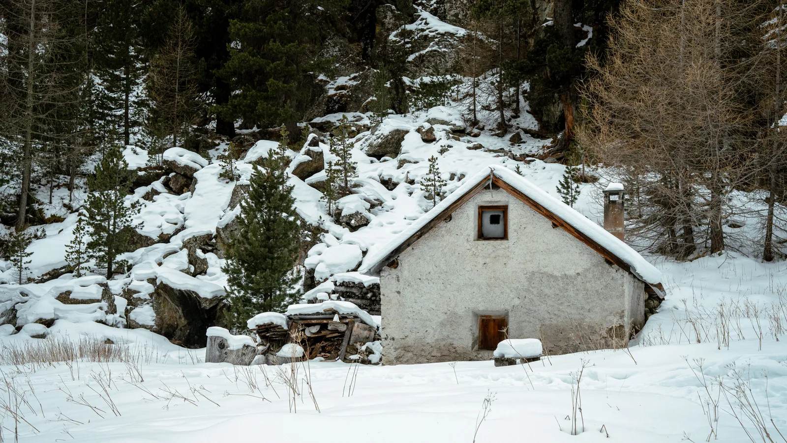 A small stone mountain hut in deep snow among pine trees