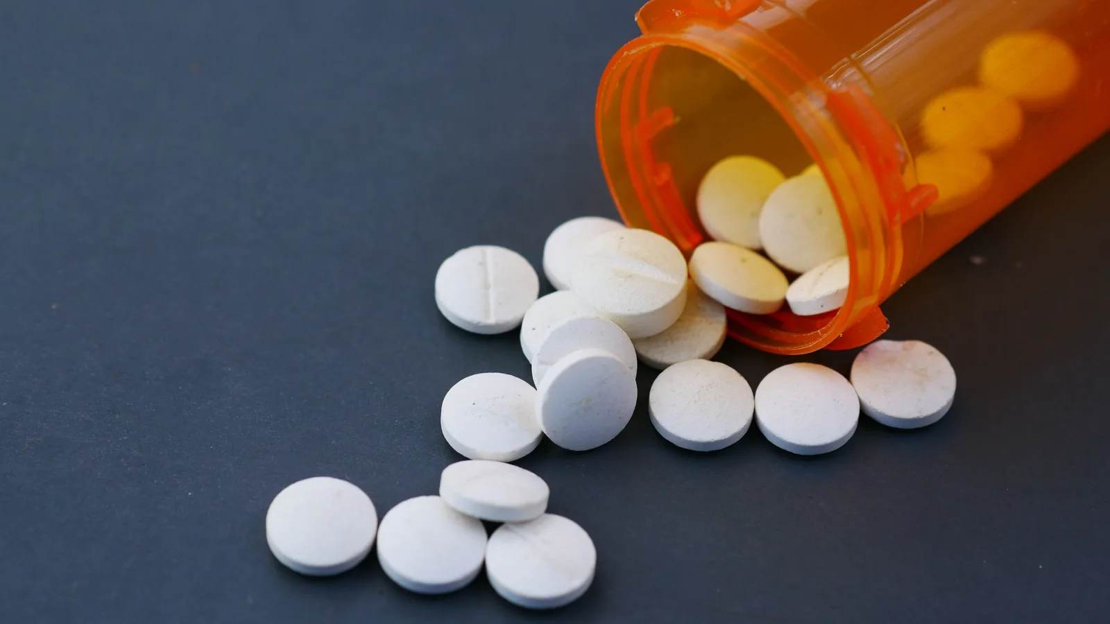 White tablets spilling from an orange prescription bottle