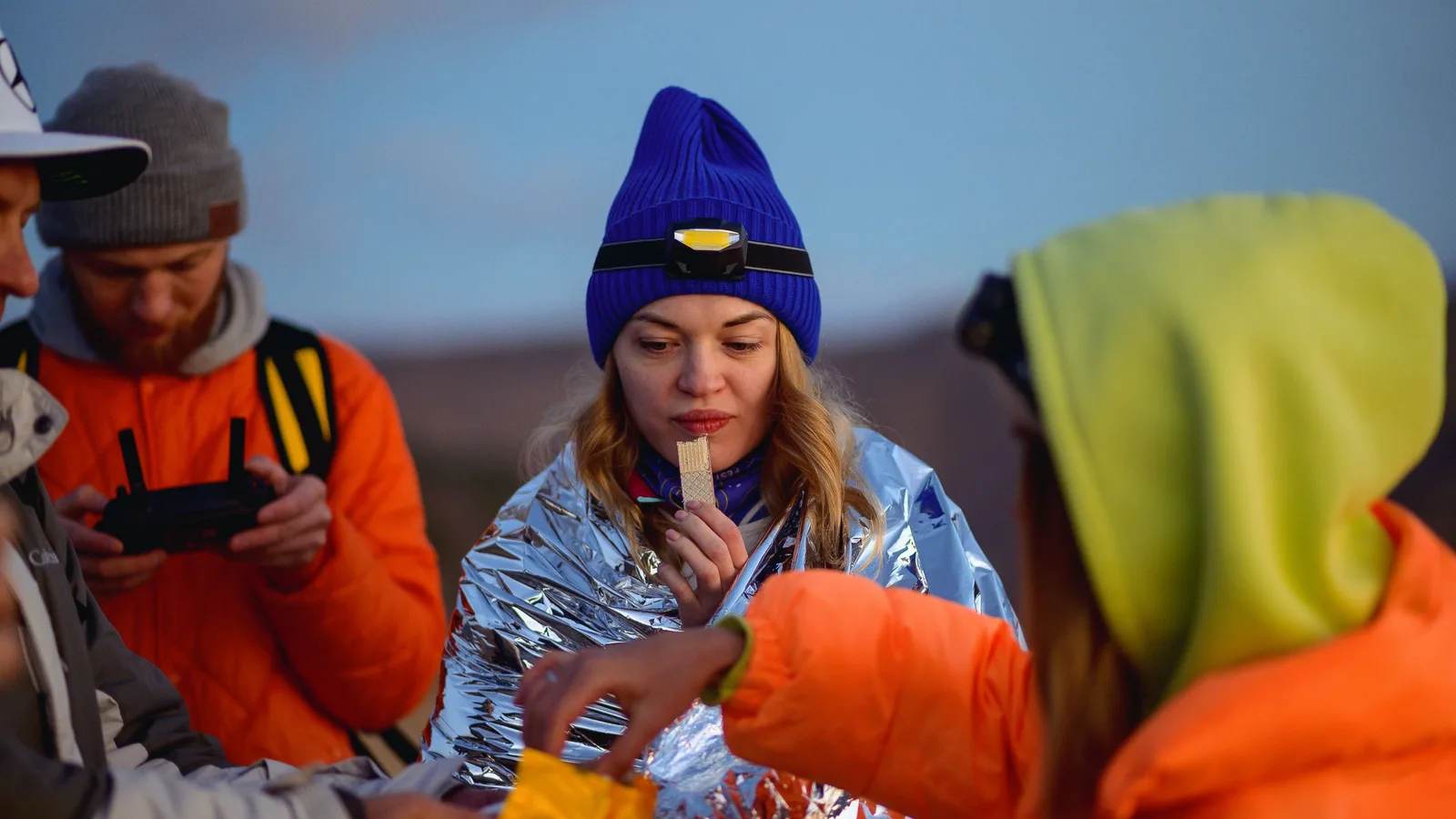 Hikers in warm jackets sharing snacks outdoors on a cold evening