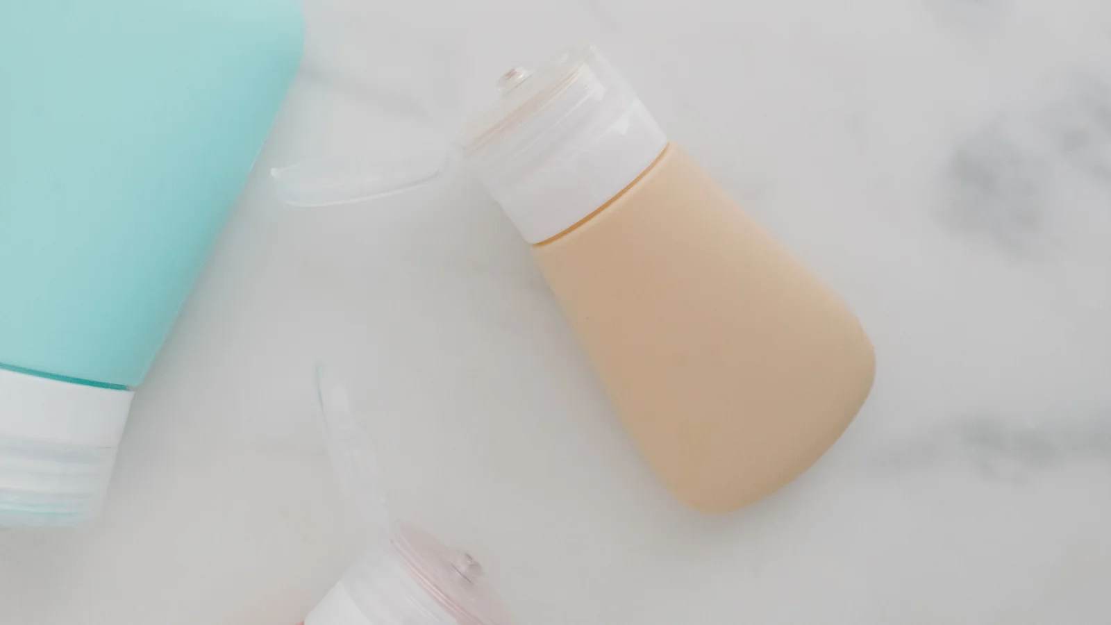 Soft-coloured refillable travel bottles with flip-top caps on a white marble surface