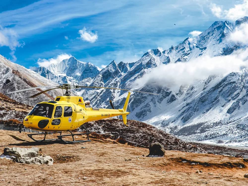 A yellow helicopter parked on a high mountain landing