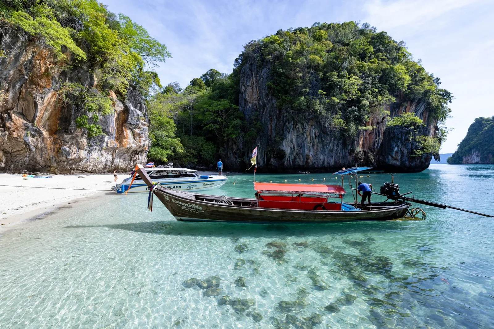 A turquoise tropical bay with limestone karst islands and a wooden longtail boat in southern Thailand — an iconic Southeast Asia coast scene