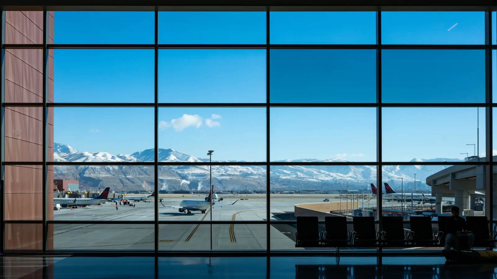 Aircraft on the apron seen through an airport terminal window, snow-capped mountains beyond