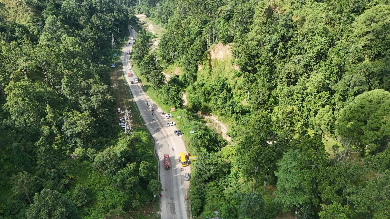 An excavator works a cut slope above a two-lane hill highway in Nepal. A representative view of the terrain the Prithvi Highway crosses, not the Krishnabhir site itself.