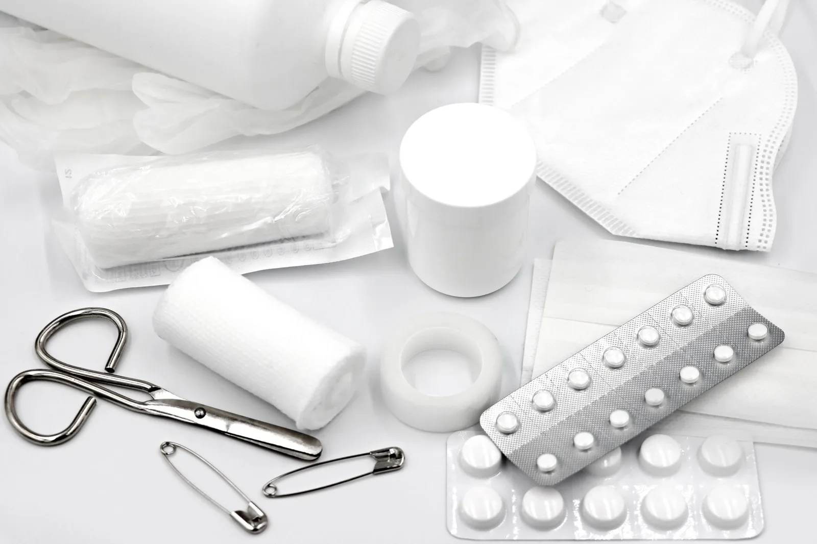An open travel first-aid kit with plasters, bandages, medicines and tools laid out on a surface