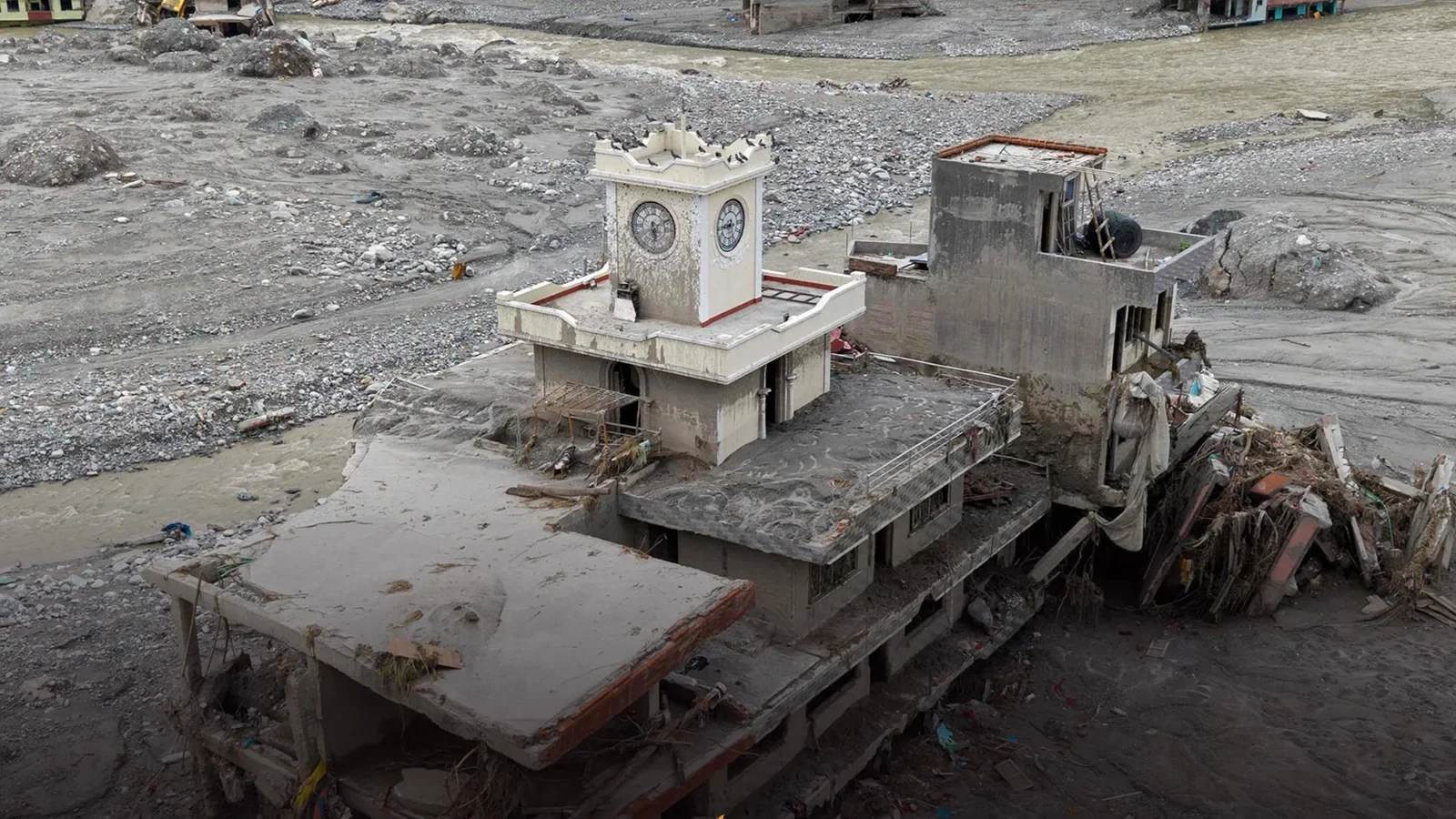 A clock tower left standing on a collapsed slab in a plain of grey flood silt on the Trishuli, after the 26 August 2026 Bhote Koshi flood. Photograph shared on Instagram.
