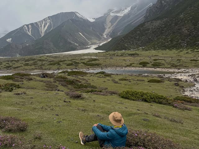 Trekker resting on a meadow above a glacial valley near Samagaon